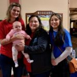 Three staff smiling and one holding a baby