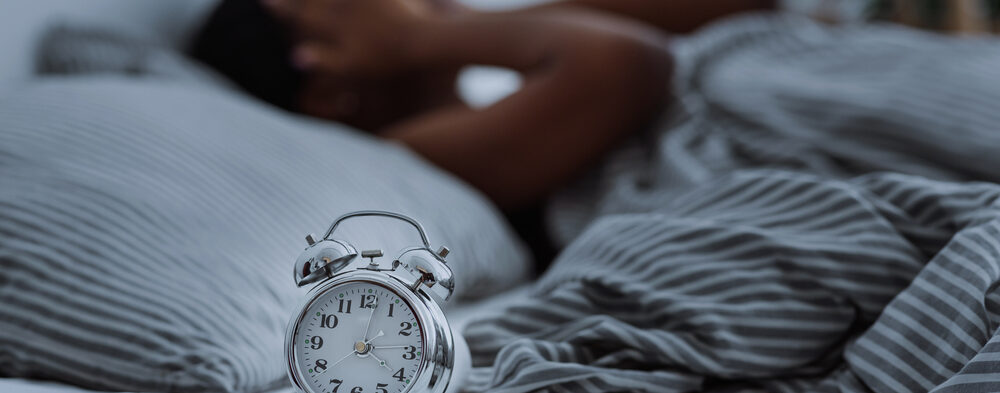 person lying in bed without sleep with alarm clocks close up.