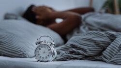 person lying in bed without sleep with alarm clocks close up.